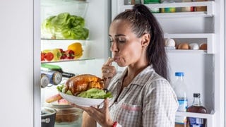 Frau steht mit gebratenem Hühnchen vor dem Kühlschrank