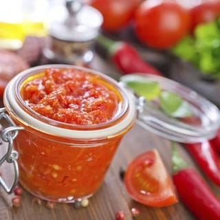 Tomatensauce im Glas, dekoriert mit Tomatenstücken und Chilischoten