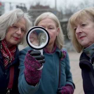 Drei Damen auf der Suche mit einer Lupe