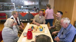 US Marines aus Böblingen zu Besuch in einem Altenheim in Zuffenhausen. Sie sitzen am Tisch und spielen mit Bewohnern Mensch-ärgere-dich-nicht.