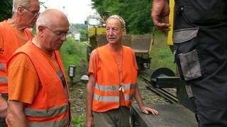 Männer des Fördervereins Welzheimer Bahn reparieren die Zugstrecke nach Welzheim. Sie tragen orangene Warnwesten.
