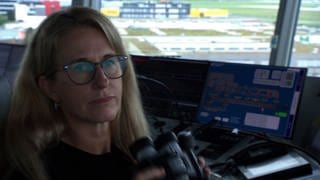 Fluglotsin Carola End sitzt mit einem Fernglas in der Hand im Tower des Flughafens Stuttgart