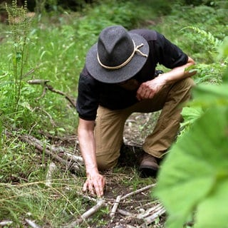 Survival-Profi Ralf Greiner ist Fährtenleser. Er kniet auf dem Waldboden und schaut sich eine Tierspur an.