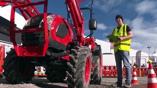 Ein Mann mit Warnweste steht neben einem roten Traktor auf der Oberschwabenschau in Ravensburg.