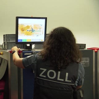 Zwei Zollbeamte beim scannen eines Koffers