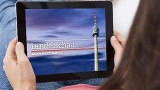 Eine Frau sitzt mit ihrem Tablet-PC auf der Couch und schaut sich eine Sendung der Landesschau Baden-Württemberg an.