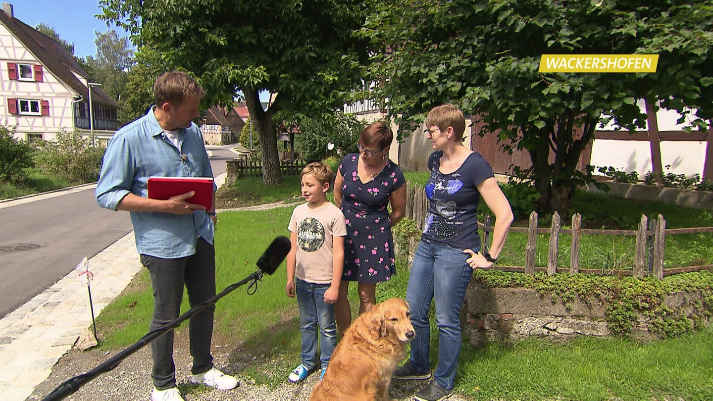 Moderator Jens Hübschen auf einem Dorfplatz mit Kind, zwei Frauen und einem Hund