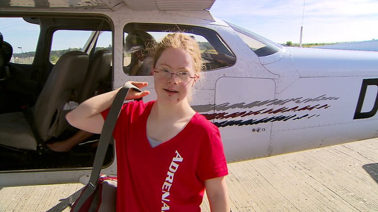 Kind mit Downsyndrom steht vor Flugzeug