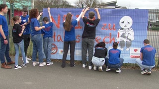 Jugendliche hängen ein Banner mit der Aufschrift "Nein zu Hatespeech" an einen Zaun