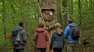 Vier Wanderer stehen staunend vor einem Gandalf aus Holz auf dem Auenlandweg