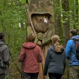 Vier Wanderer stehen staunend vor einem Gandalf aus Holz auf dem Auenlandweg