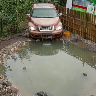 Die Handwerksprofis bauen ein altes Auto in einen Brunnen mit Teich um