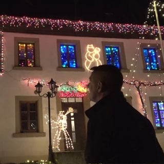 Mann vor Haus das voller Lichterkettendeko ist