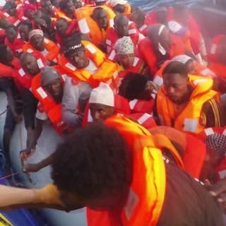 Schlauchboot voller Flüchtlinge wird von Rettungsschiff längsseite genommen. Flüchtling wird an Bord geholt