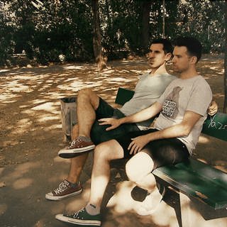 Schwules Paar sitzt auf einer Bank an einem Waldweg