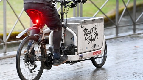 Lastenfahrrad: Jemand fährt mit einem Lastenfahrrad mit der Aufschrift "Ich ersetze ein Auto"