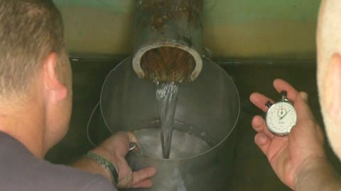 Zwei Wassertechniker messen die Durchflussmenge am Auslauf einer Quelle