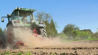 Traktor zieht Staubfahne hinter sich her. Vertrockneter Acker.