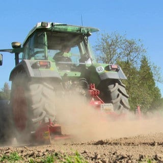 Traktor zieht Staubfahne hinter sich her. Vertrockneter Acker.