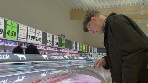 Mann im Supermarkt, sucht in der Kühltheke nach Fleisch-Produkten