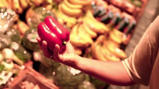 Eine Frau im Supermarkt hält eine Paprika in der Hand