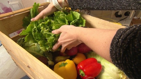 Frau greift in eine Holzkiste mit frischem Gemüse und einem großen Salatkopf