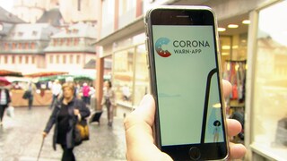 Handy mit Corona Warn-App auf dem Bildschirm wird rechts ins Bild gehalten