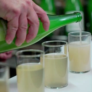 Aus einer grünen Glasflasche wird milchig-trüber Federweißer ausgeschenkt.