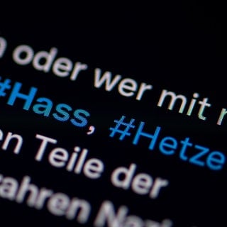 Auf dem Bildschirm eines Smartphones sieht man die Hashtags Hass und Hetze in einem Twitter-Post.