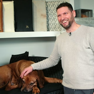 Björn Wiltholt neben einem braunen Hund auf einem Hundebett.