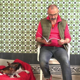 Künstler Hermann Weber sitzt mit seinem Hund Bruno vor einer gemusterten Fliesenwand.