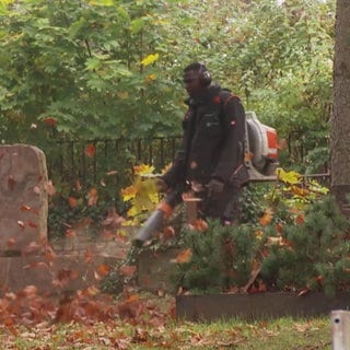 Ein Mann bläst Laub auf einem Friedhof