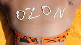 Eine junge Frau hat den Schriftzug "Ozon" aus Sonnencreme auf ihrem Rücken stehen. 