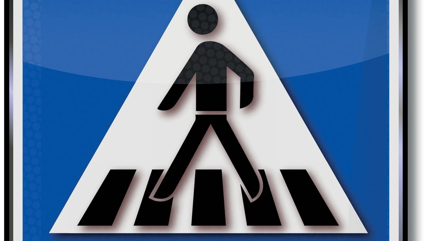 Auf einem blauen Schild ist ein weißes Dreieck abgebildet. Auf diesem Dreieck überquert ein schwarzer Mann mehrere schwarze Streifen. Es handelt sich um das Schild, das einen Fußgängerüberweg ausweist, umgangssprachlich auch Zebrastreifen genannt.