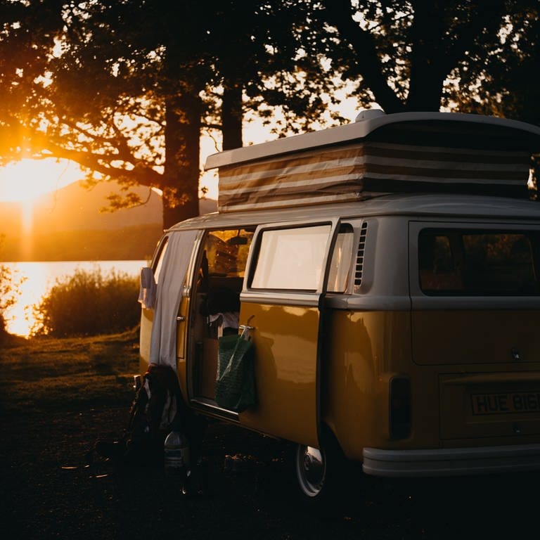 Alter Camperbus mit englischem Kennzeichen steht an einem See während die Sonne untergeht.
