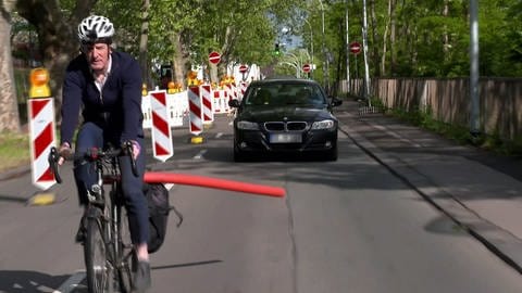 Ein Radfahrer fährt vor einem Auto: Fahrradfahrende dürfen innerorts nur mit 1,50 Metern Abstand überholt werden - praktisch heißt das oft: Überholverbot für Autofahrende.