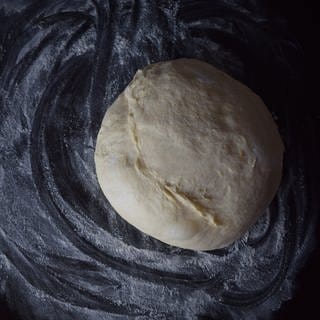 Roher Pizzateig auf schwarzem Hintergrund, Pizzateigrezept für zu Hause