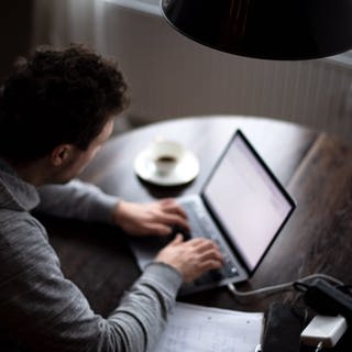 Ein Mann sitzt im Homeoffice am Tisch an einem Laptop und arbeitet.