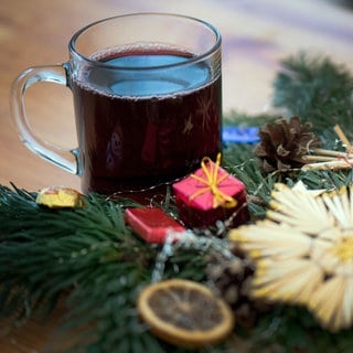 Ein Glas roter Glühwein steht neben einem Weihnachtsgesteck.