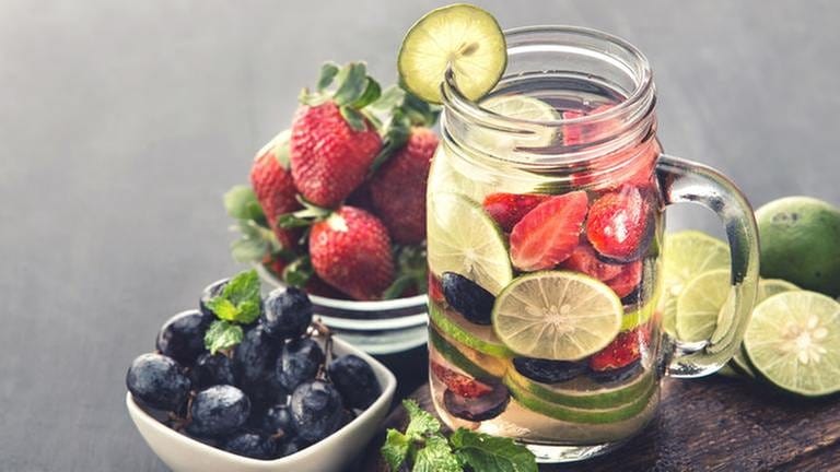 Eine Glas Wasser mit Limetten, Erdbeeren und Heidelbeeren.