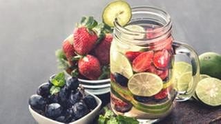 Eine Glas Wasser mit Limetten, Erdbeeren und Heidelbeeren.