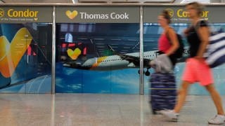 Passagiere gehen neben einem großen Werbeschild von Thomas Cook am Flughafen von Palma de Mallorca.