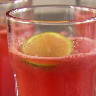Hellrotes Getränk mit Limettenscheibe in Glas. Für dieses gesunde Smoothie Rezept braucht man Wassermelone, Apfelschorle, Zitrone oder Limette und Minze
