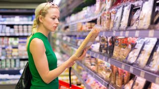 Eine Frau betrachtet im Supermarkt eine Lebensmittelverpackung.
