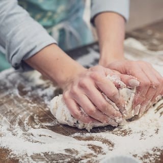 Zwei Hände kneten auf einer Arbeitsplatte Teig mit viel Mehl. Brotbackmischungen im Test: Welche Backmischung ist die beste?