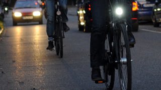 Ein Fahrrad mit Beleuchtung und eines ohne Licht fahren im Dunkeln nebeneinander