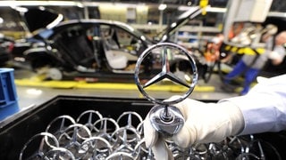 Ein Mitarbeiter hält ein Emblem der Automarke Mercedes-Benz