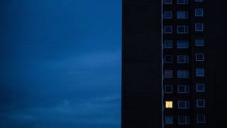 In einem Hochhaus vor dunklem Himmel ist nur ein Fenster beleuchtet. Die Preisbremse bei Strom und Gas soll Verbraucher entlasten. Wie kann man Geld sparen?