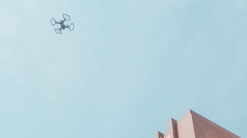 Drohne fliegt am Himmel über eckigem Gebäude. Wie viel sollte eine vernünftige Drohne kosten und wer darf sie fliegen?