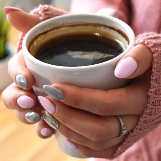 Wie gefährlich ist zu viel Kaffee? Frau hält eine Tasse Kaffee in der Hand.